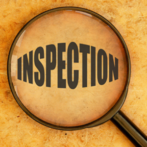 A sanitation worker in a white hazmat suit uses a pressure sprayer to disinfect a wooden bench in an office.